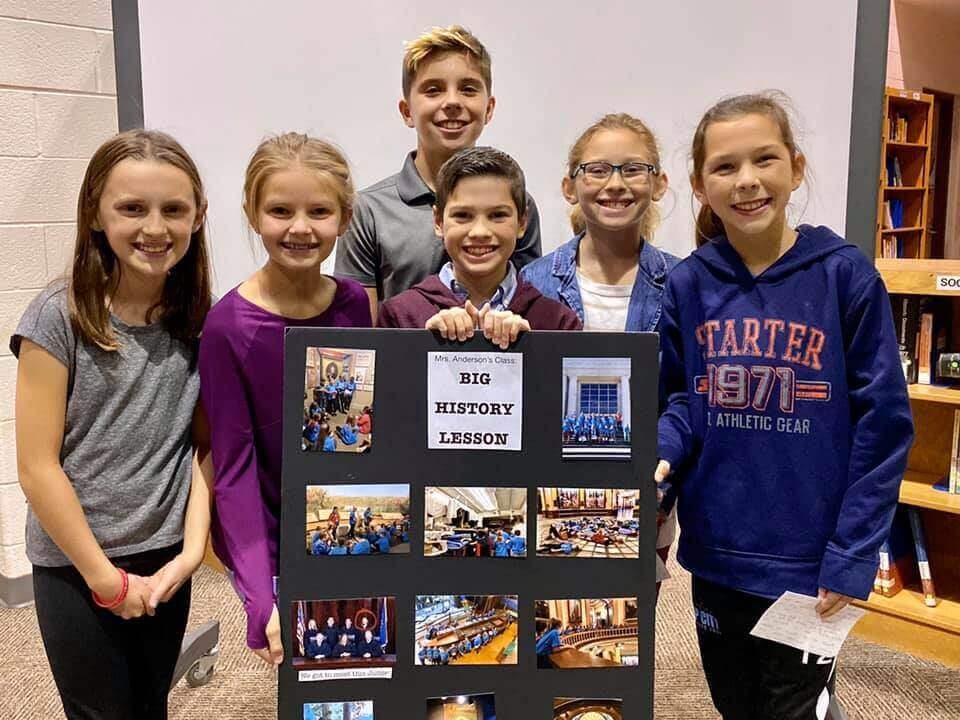 Group of six students standing around a poster board reading "Big History Lesson"