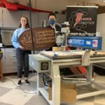 Two students holding a large wooden sign with Laingsburg Educational Advancement Foundation carved into it.