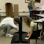 Two students fixing a table that is on the ground upside down.