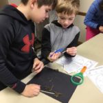 Two young boys using a magnifying glass for a science project.