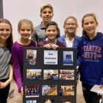 Six children posing with a poster board reading "Big History Lesson" with pictures.