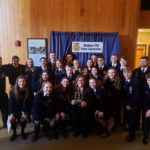 A group of well-dressed students surrounding a teacher holding a plaque at the Michigan FFA State Convention.