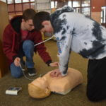 Two children performing CPR on a CPR dummy.