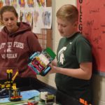 A student holding a robotic car standing next to a teacher.