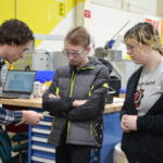 Three teenage students standing around engineering materials together.
