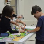 A group of young students standing around a table playing with Lego robotics.