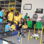 Three groups of students wearing color coordinated T-shirts battling their robotics.