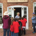 A group of students and counselors or teachers huddled around the outside of a General Store.