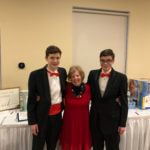 Two young men in tuxedos and red bowties on either side of an older woman wearing a red dress.