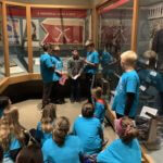 Students wearing blue school shirts standing in a history museum exhibit.