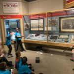 Students wearing blue school shirts standing in a history museum exhibit.