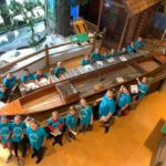 Group of young students wearing blue school shirts surrounding a large wooden canoe.