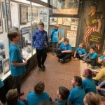 Students wearing blue school shirts standing in a history museum exhibit.