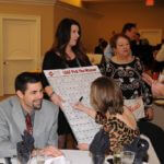 Woman holding a poster board while those around her sign the poster board and ask her questions.