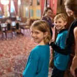 Young students in blue shirts smiling in a historic room.