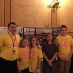 A group of young students with a teacher standing in front of a trifold poster board reading "Student Centered Learning."