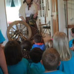 Group of young students sitting down and watching a presenter with a ship's steering wheel.