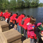 Group of students wearing red shirts looking out at a lake.