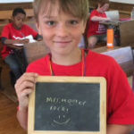 Young student with a chalk board reading "Mrs. Hoover Rocks."