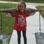 Young girl balancing two buckets on a pole over her shoulders.