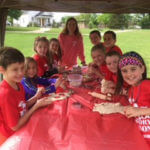 A group of young students and a teacher wearing red T-shirts and sitting at a picnic table.