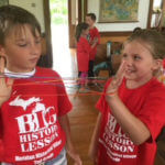 Two young students wearing coordinating red shirts playing with yarn.