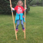 Young student with a red shirt and blue jacket walking on short stilts.