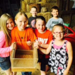 Group of young students huddled together showing off the contents of a wooden box.