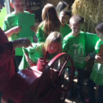 Several young students wearing green shirts operating a large piece of machinery.