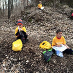 Two students sitting in the woods with notebooks.