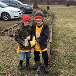 Two young students in jackets and hats standing outside.