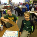 Two students sitting next to each other with a chromebook on the table in front of them.