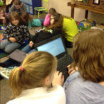 Several students sitting around a chromebook on the ground.