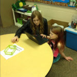 An older student and a younger student working together on a project on a chromebook.